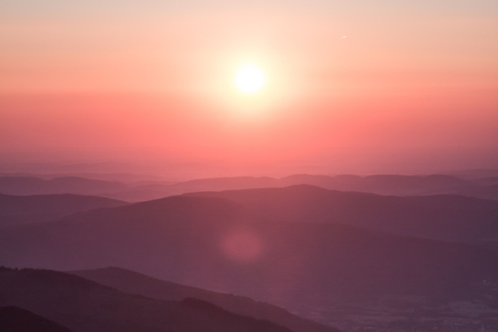 Das Bild zeigt eine rote Sonne im Hintergrund, vor der sich rote Hügel abzeichnen, die von Nebel umhüllt sind.
