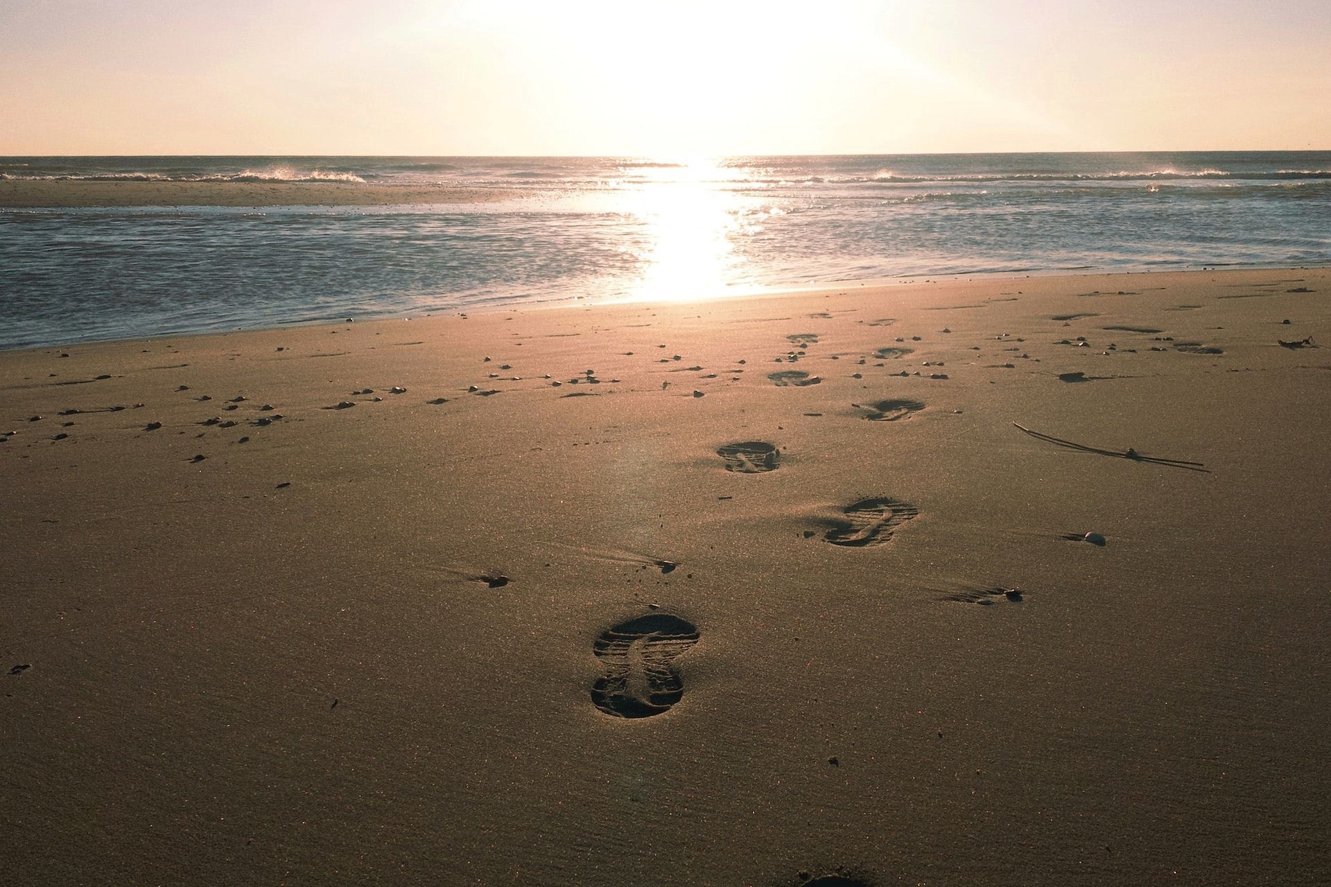 Schuhabdrücke zum Strand mit Sonnenaufgang im Hintergrund.